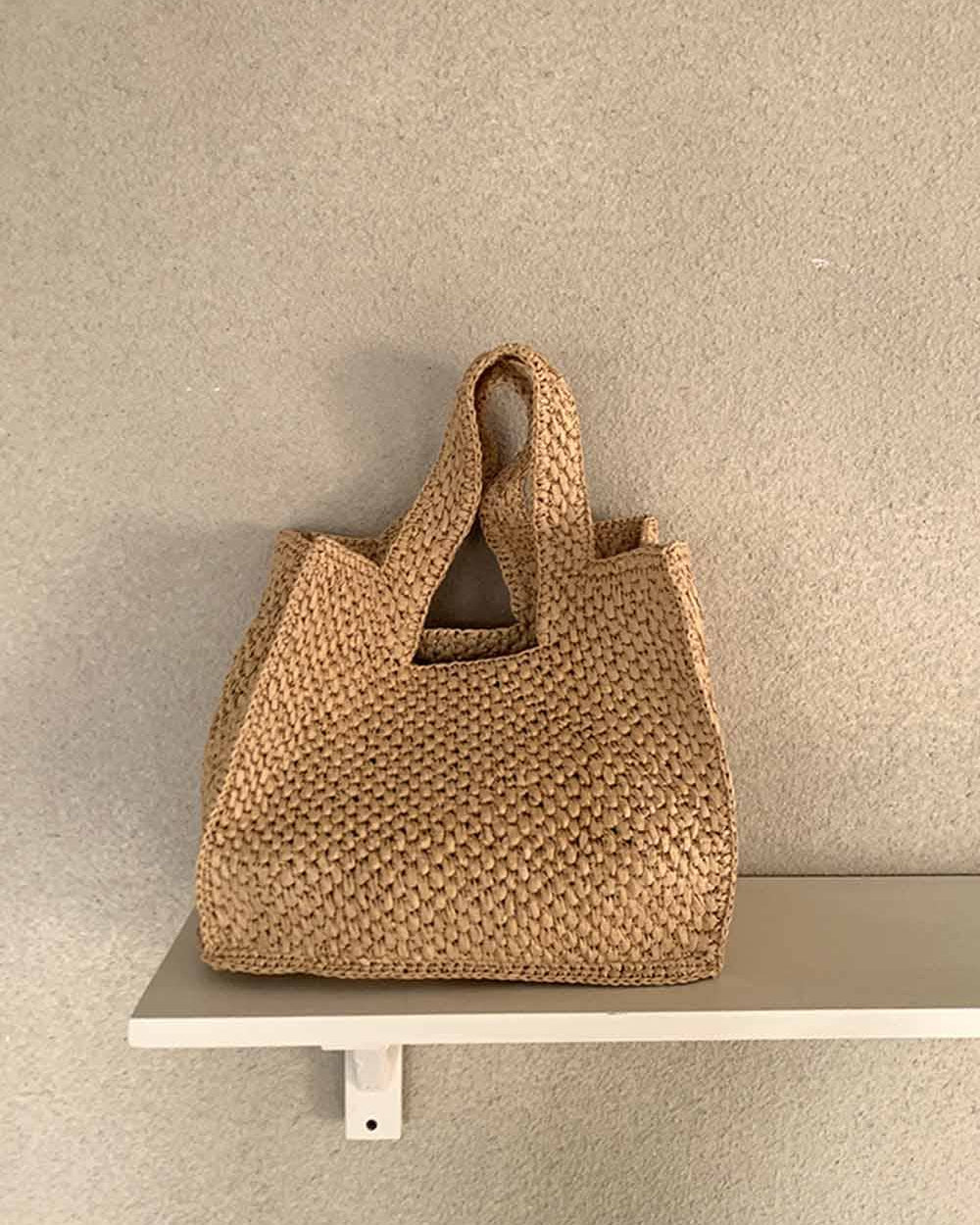 Woven brown handbag on a white shelf against a beige wall