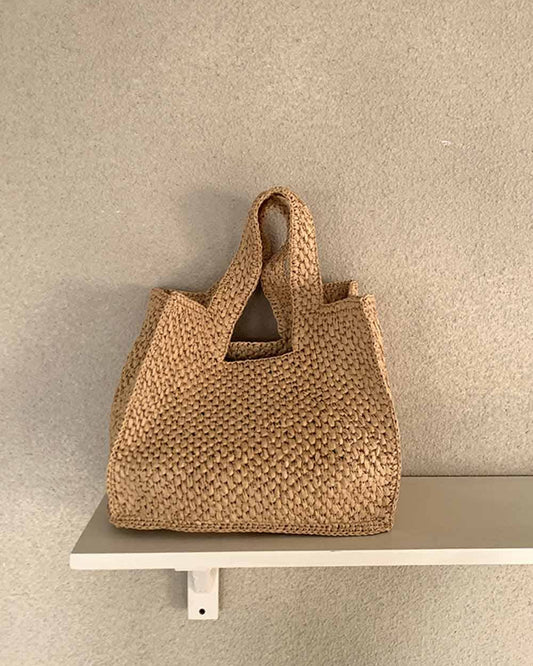 Woven brown handbag on a white shelf against a beige wall