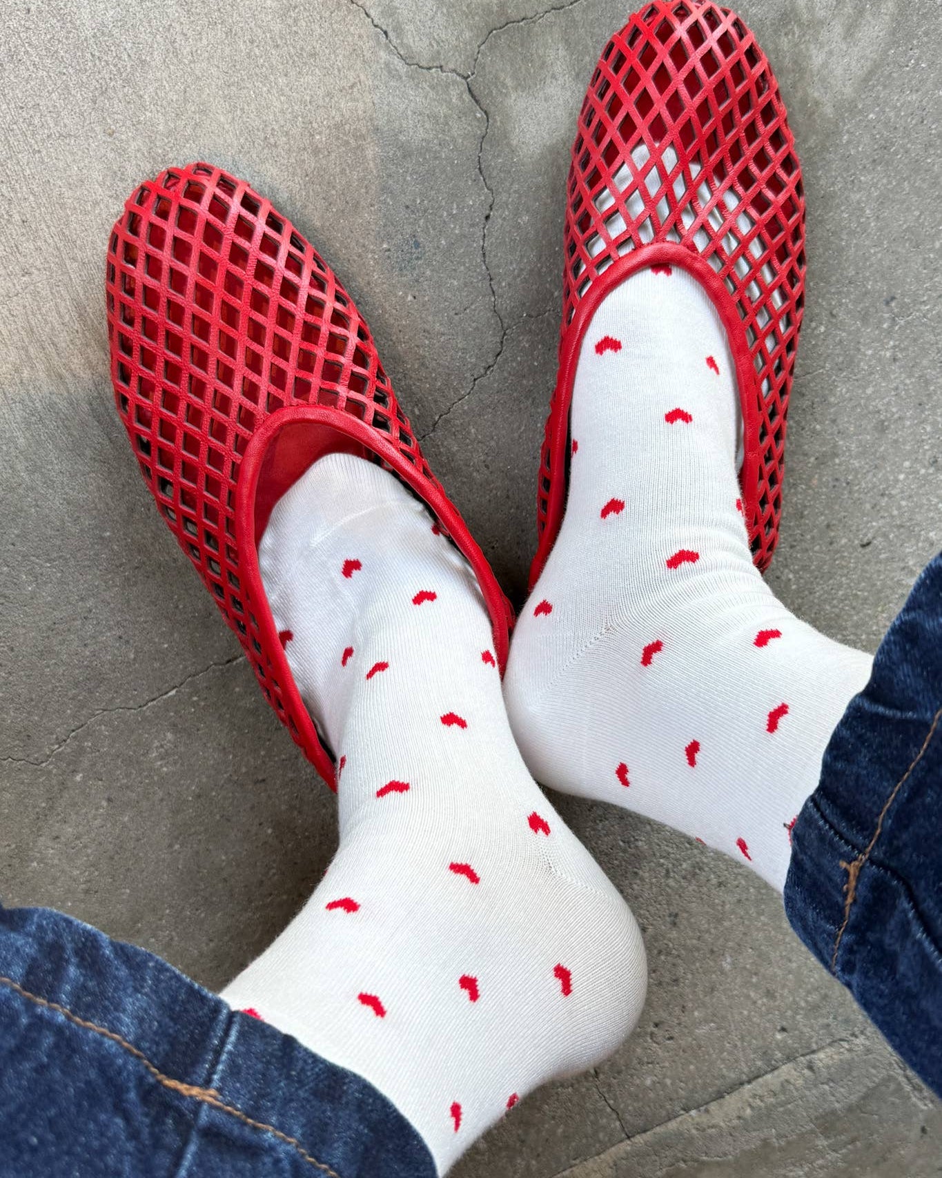 Red slip-on shoes and white socks with red polka dots on a concrete floor.