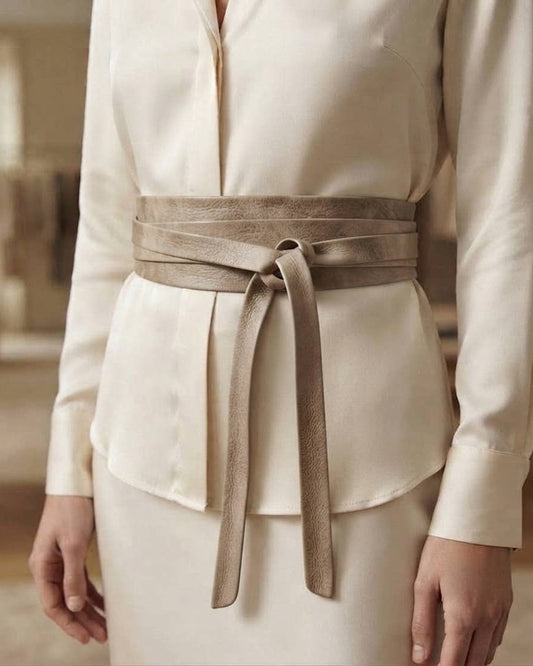 A close-up of a model wearing a cream-colored blouse and skirt with a wide taupe-brown suede belt tied at the waist.