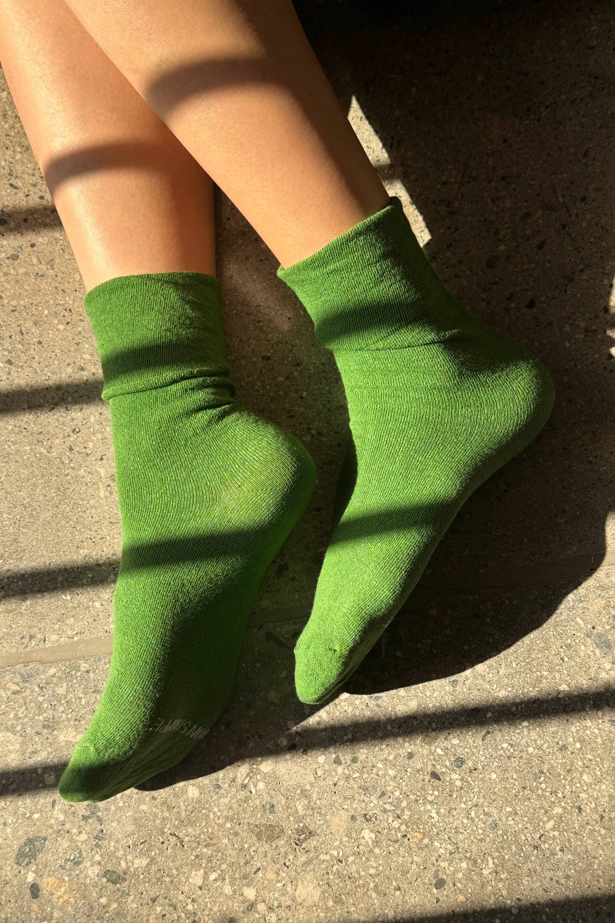 Green socks worn on a person's feet standing on a concrete surface.