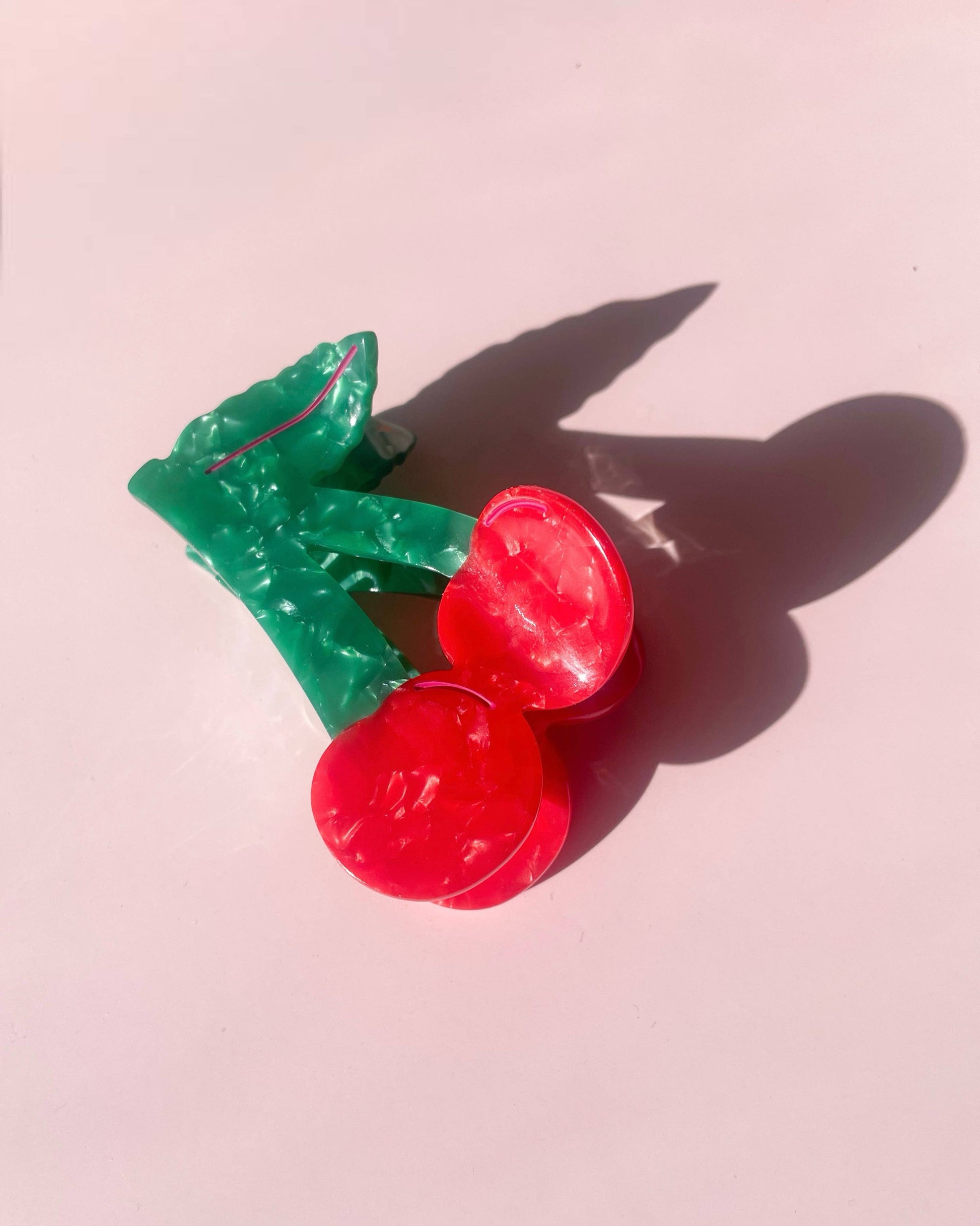 Red cherry hair clip with green leaves on a pink background