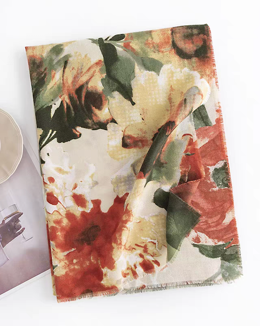 Floral patterned towel on a white surface with a cup and photo album.