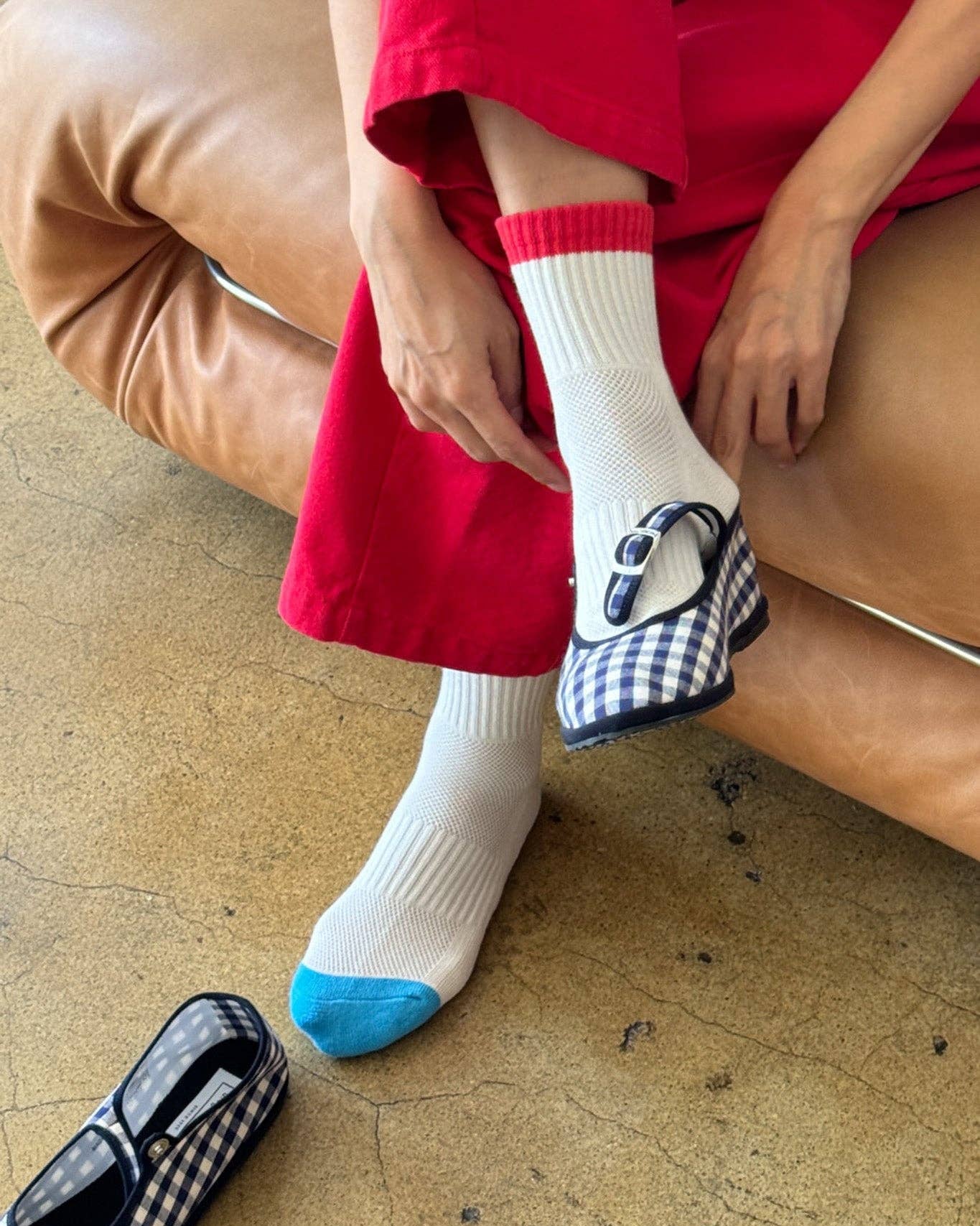 Person wearing white socks with blue toes and black and white checkered shoes on a beige floor.