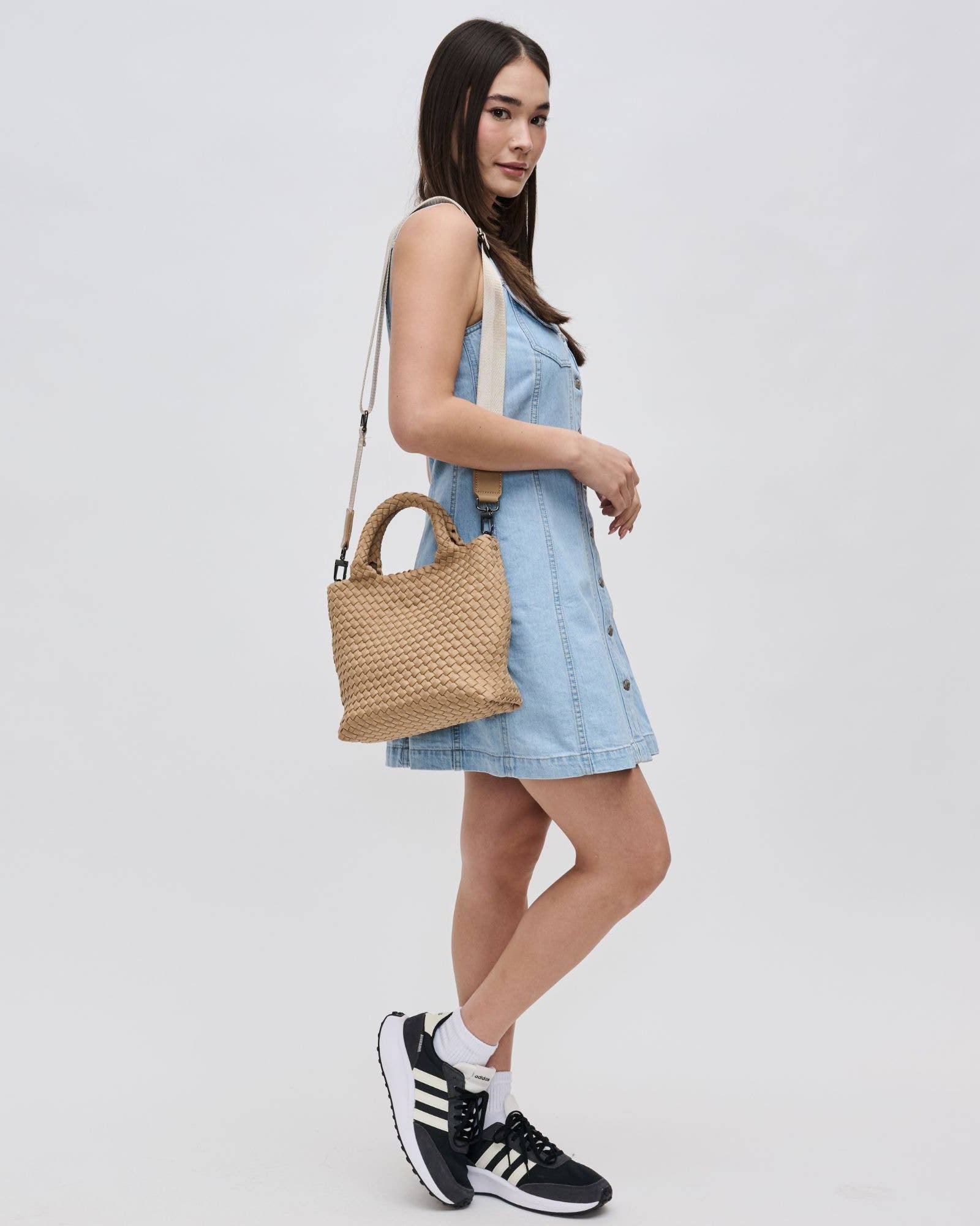 Woman in a light blue dress holding a woven handbag on a white background