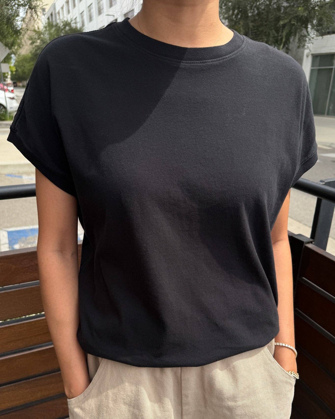 Person wearing a black t-shirt and beige pants standing outdoors.