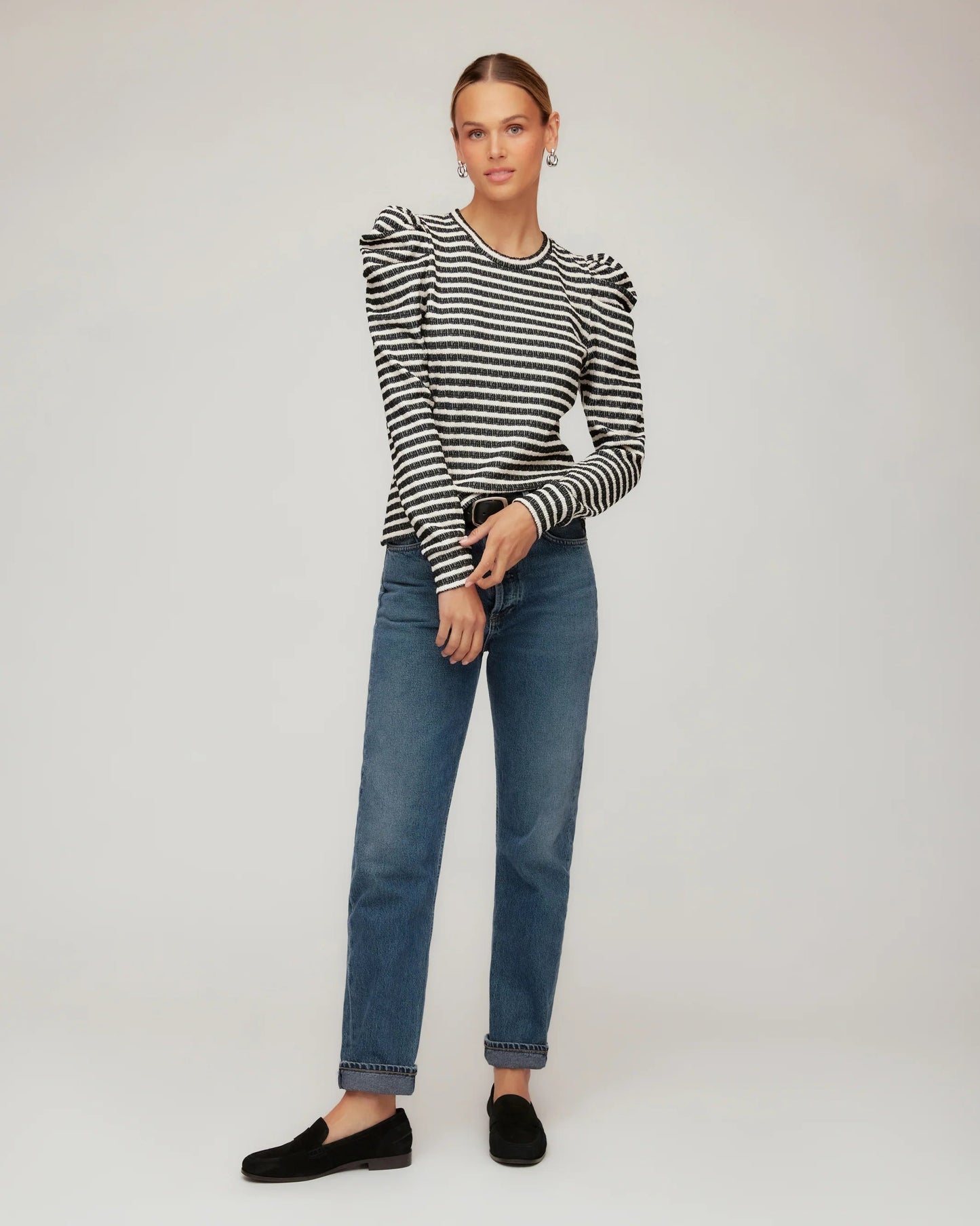 Person wearing a black and white striped sweater and blue jeans on a plain background