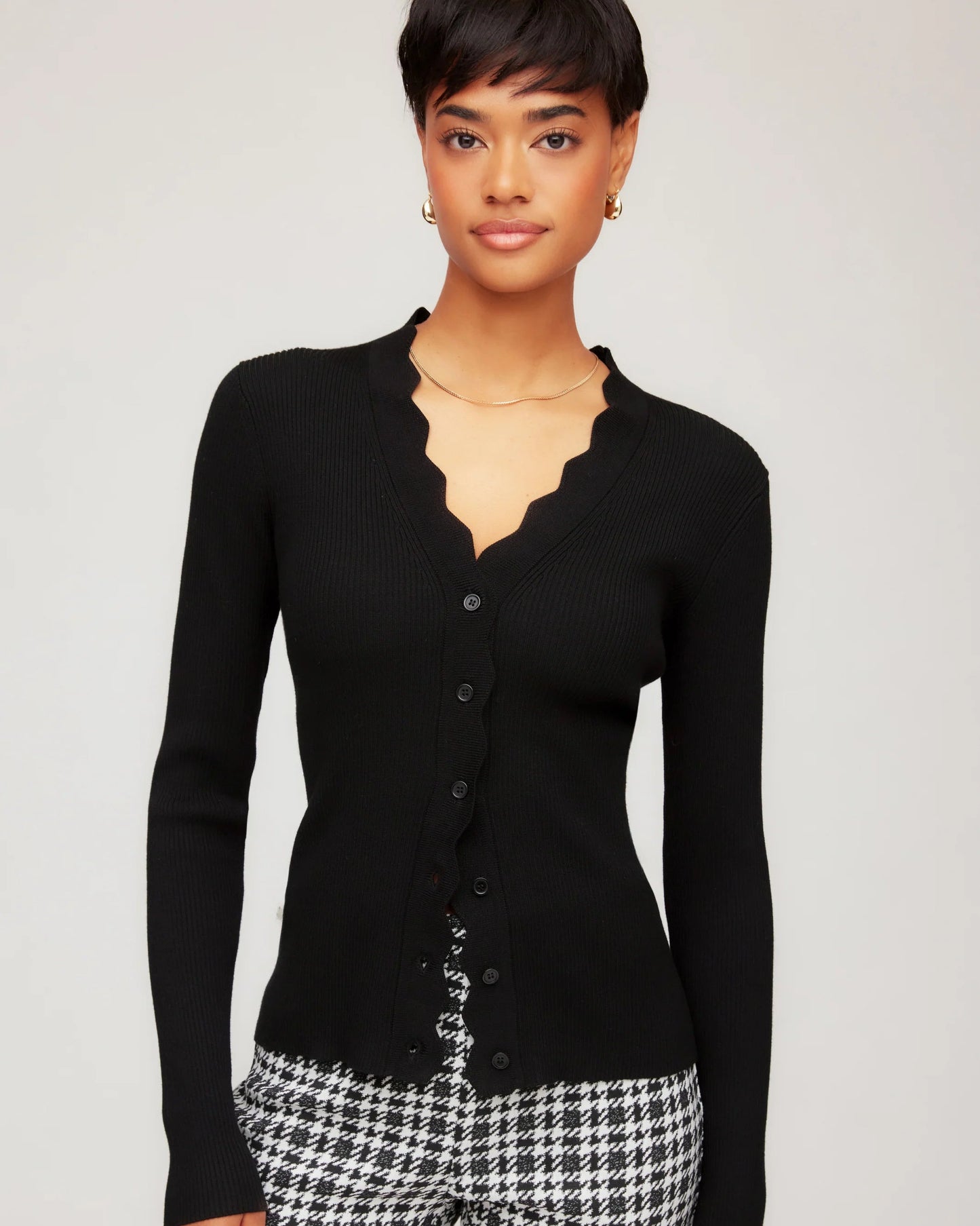 Woman wearing a black cardigan and houndstooth pattern pants on a plain background