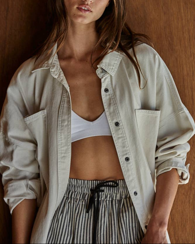 Woman wearing a light jacket over a sports bra and striped pants against a wooden background