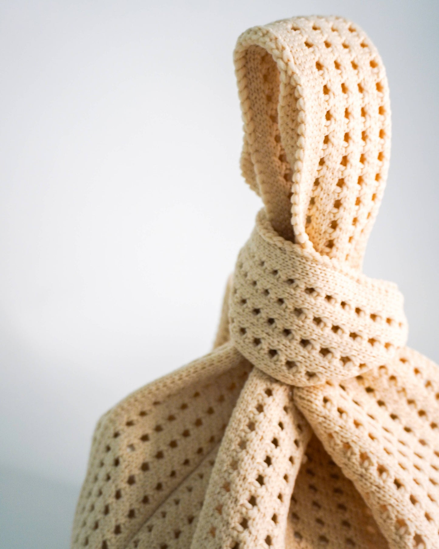 Beige knitted scarf with a knot on a light gray background
