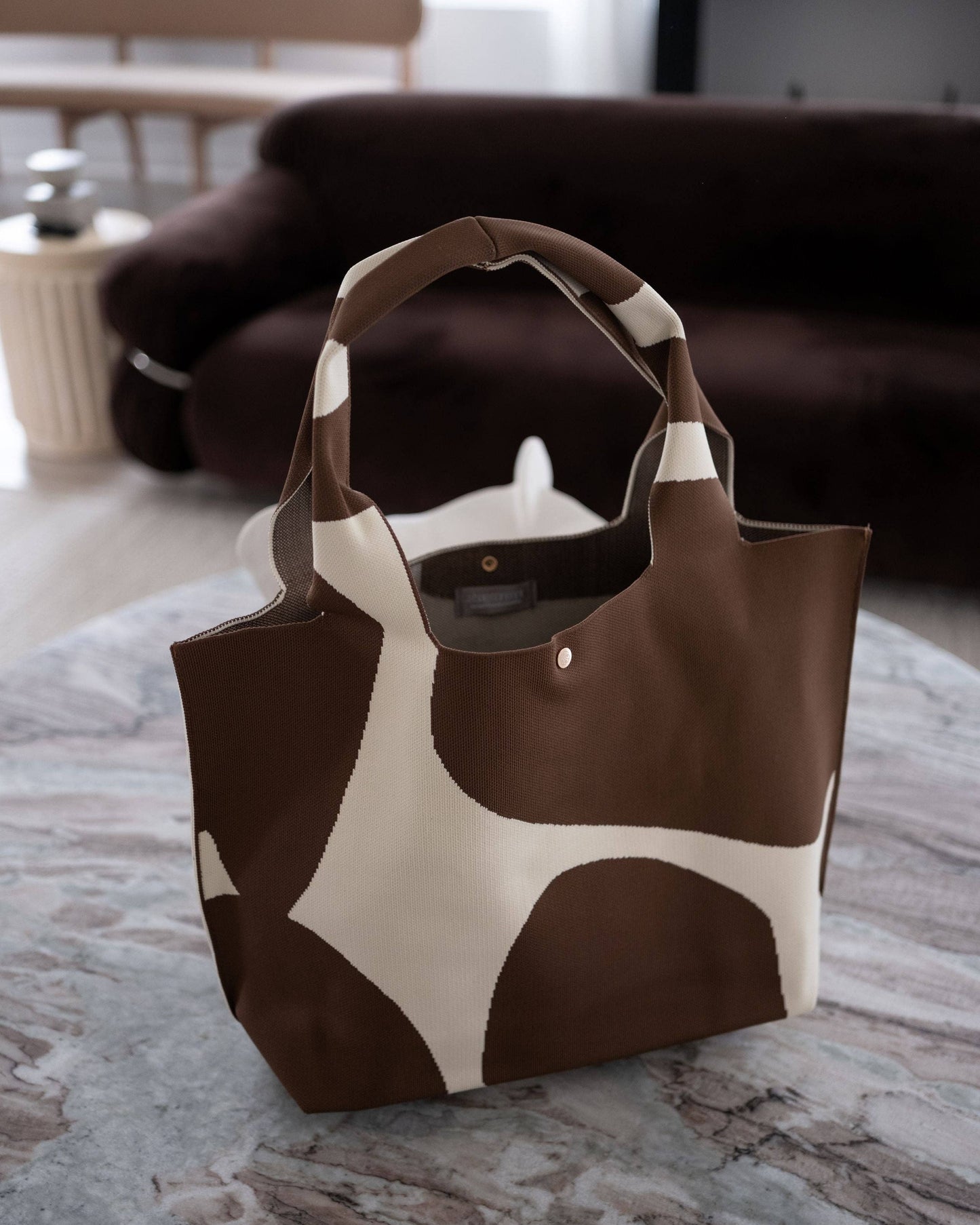 Brown and white cow print tote bag on a marble surface with a blurred indoor background