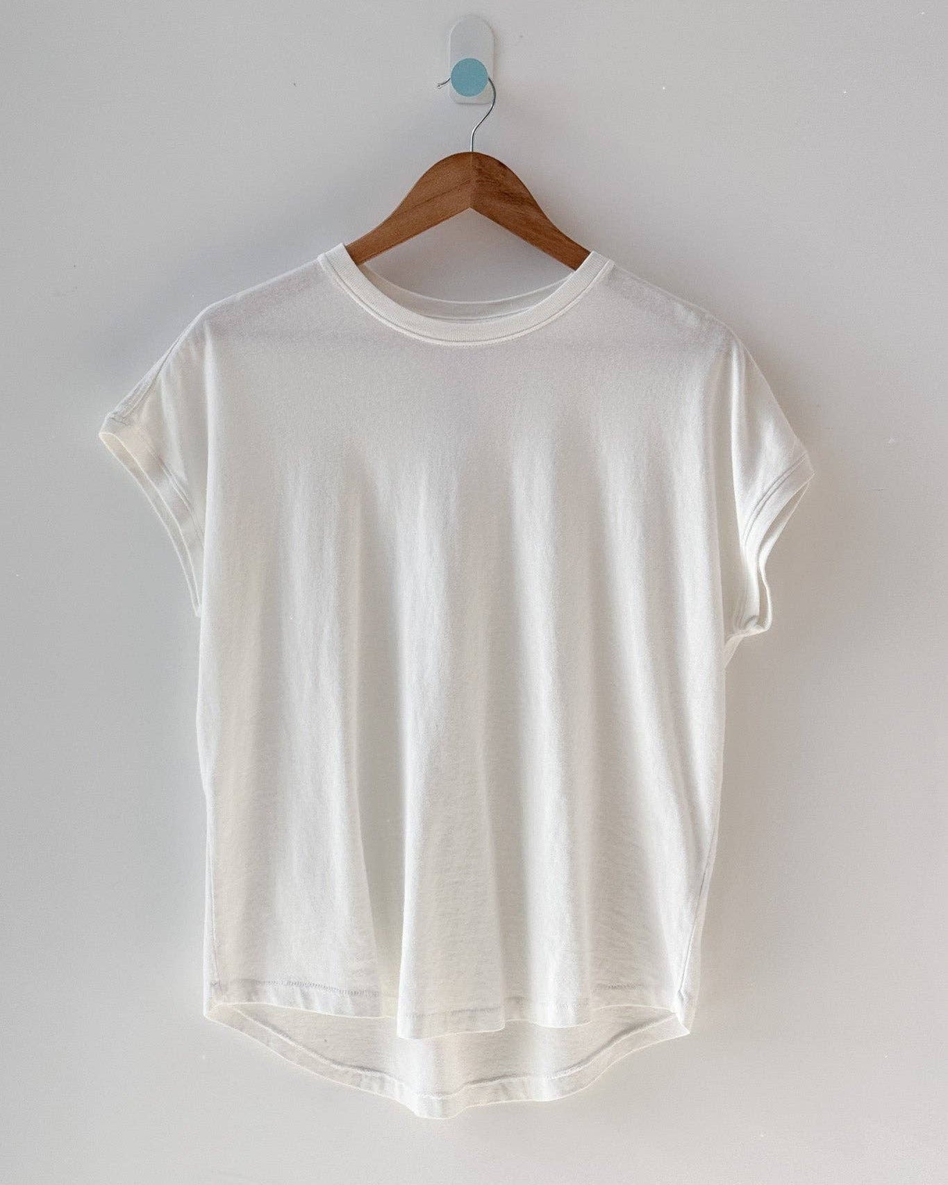 White t-shirt on a wooden hanger against a white wall