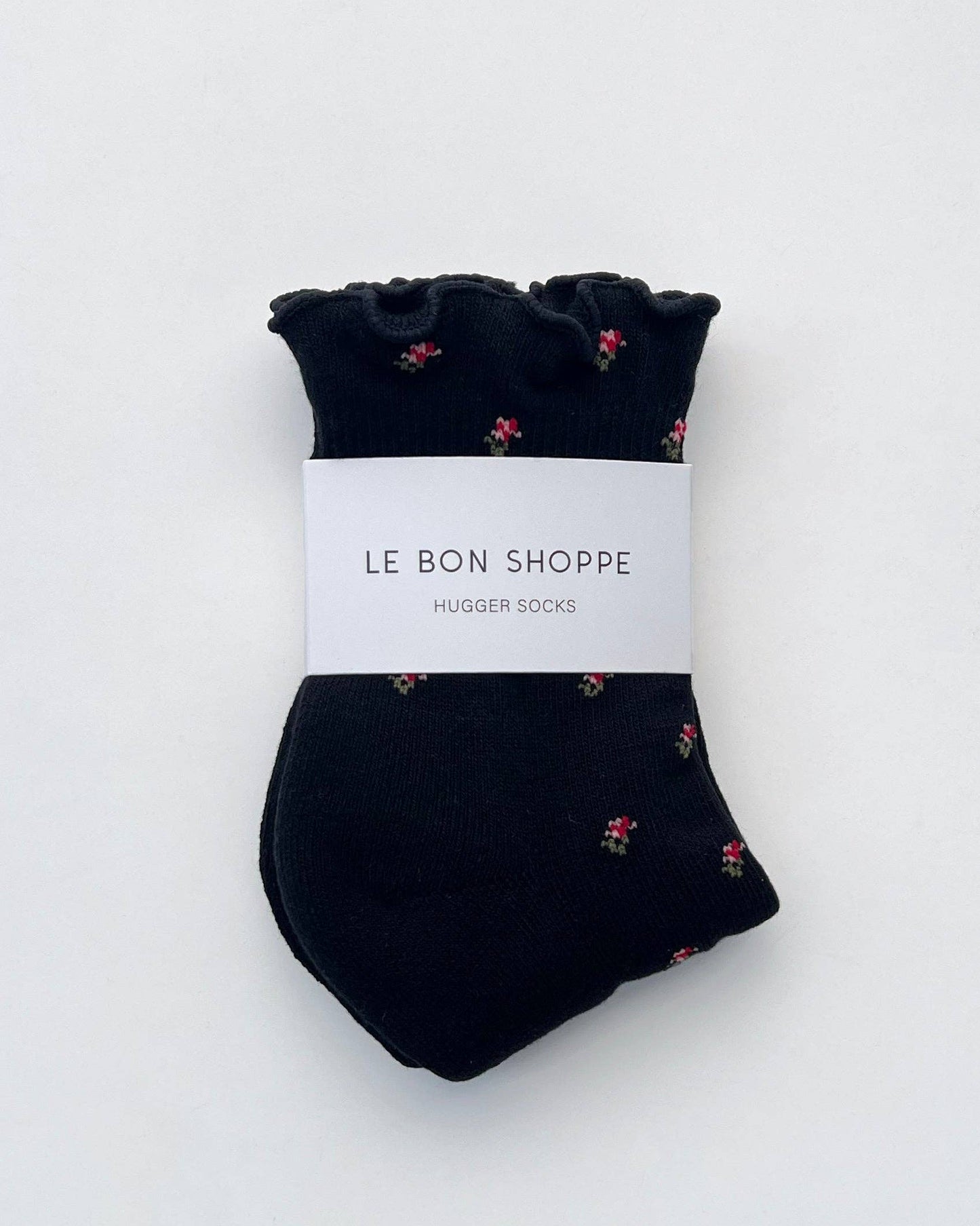 Pair of black socks with small floral pattern on a white background, branded 'Le Bon Shoppe'.