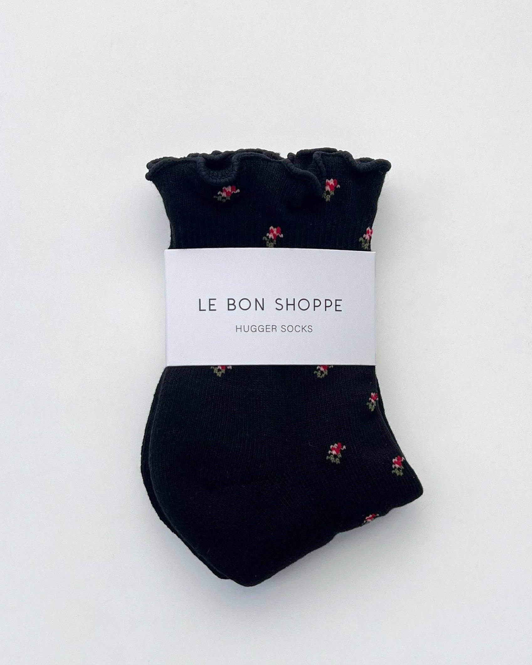 Pair of black socks with small floral pattern on a white background, branded 'Le Bon Shoppe'.