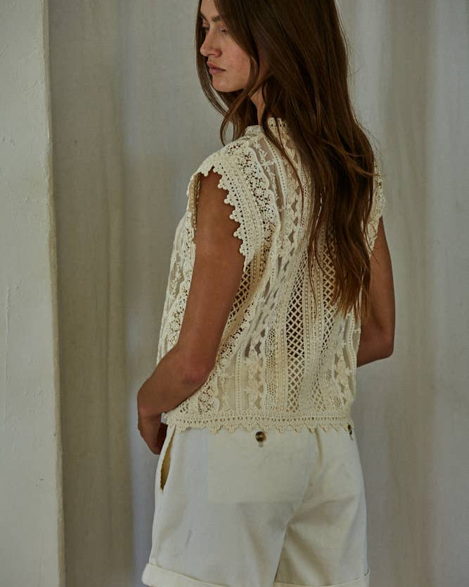 Woman wearing an off-white lace top and shorts against a plain background 