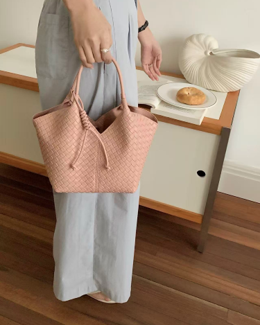 Person holding a woven pink bag in a room with a table and decorative items.