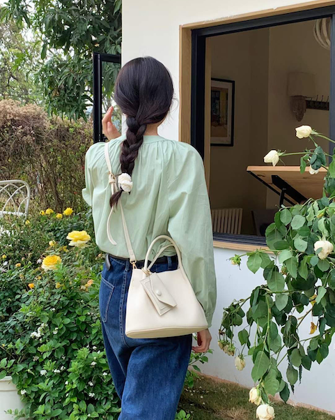 Woman with braided hair holding a white handbag, standing in a garden.