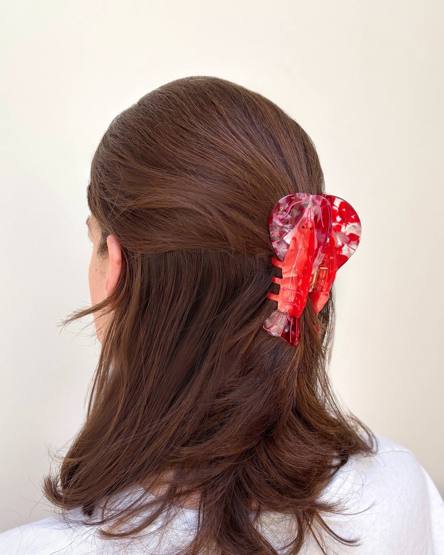 Woman with long brown hair wearing a red lobster hair clip on a plain background