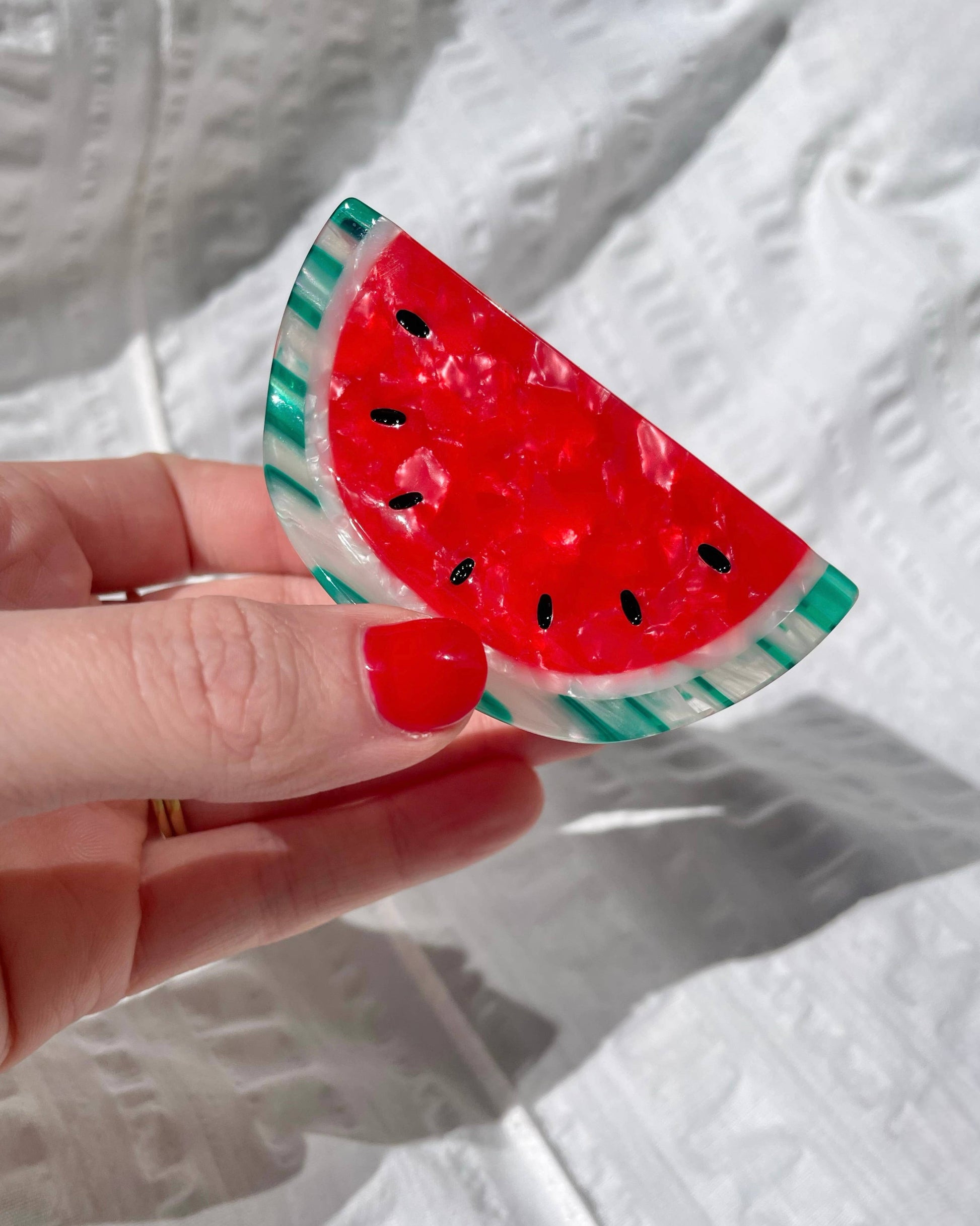 Hand holding a watermelon-shaped hairclip against a white background