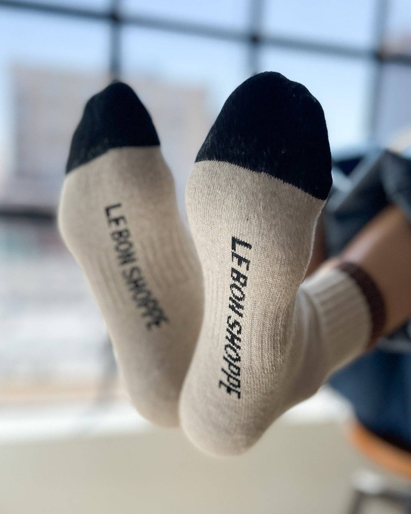 Beige socks with black toes and cuffs held up in front of a blurred indoor background