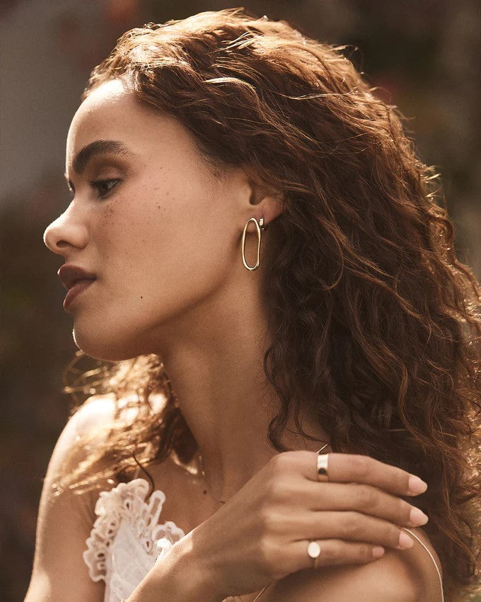 Model wearing Gorjana Gold Jagger stud earrings on a blurred background