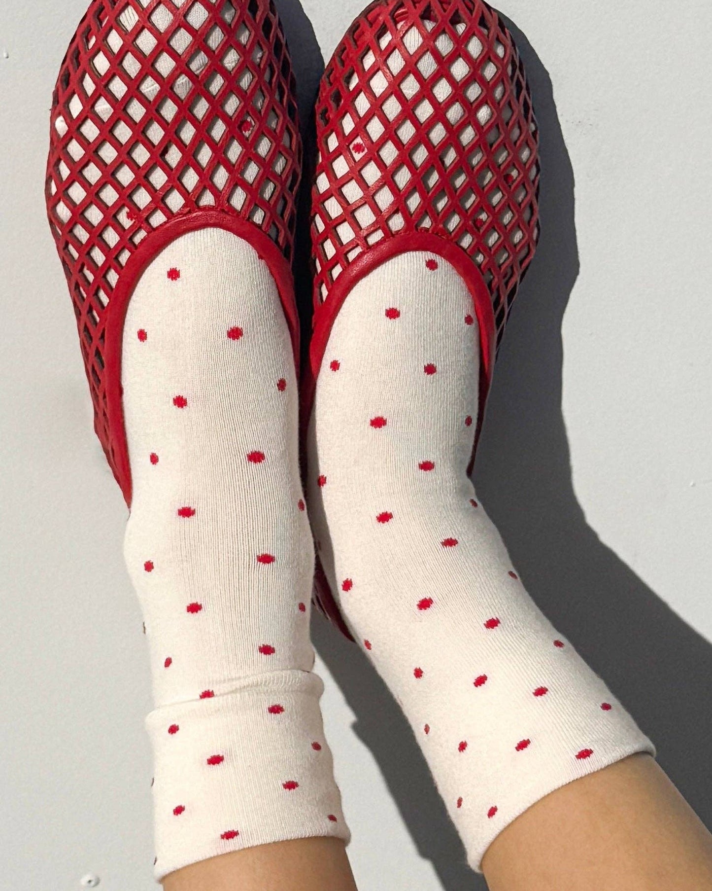 Red mesh sandals and white socks with red polka dots on a light gray background