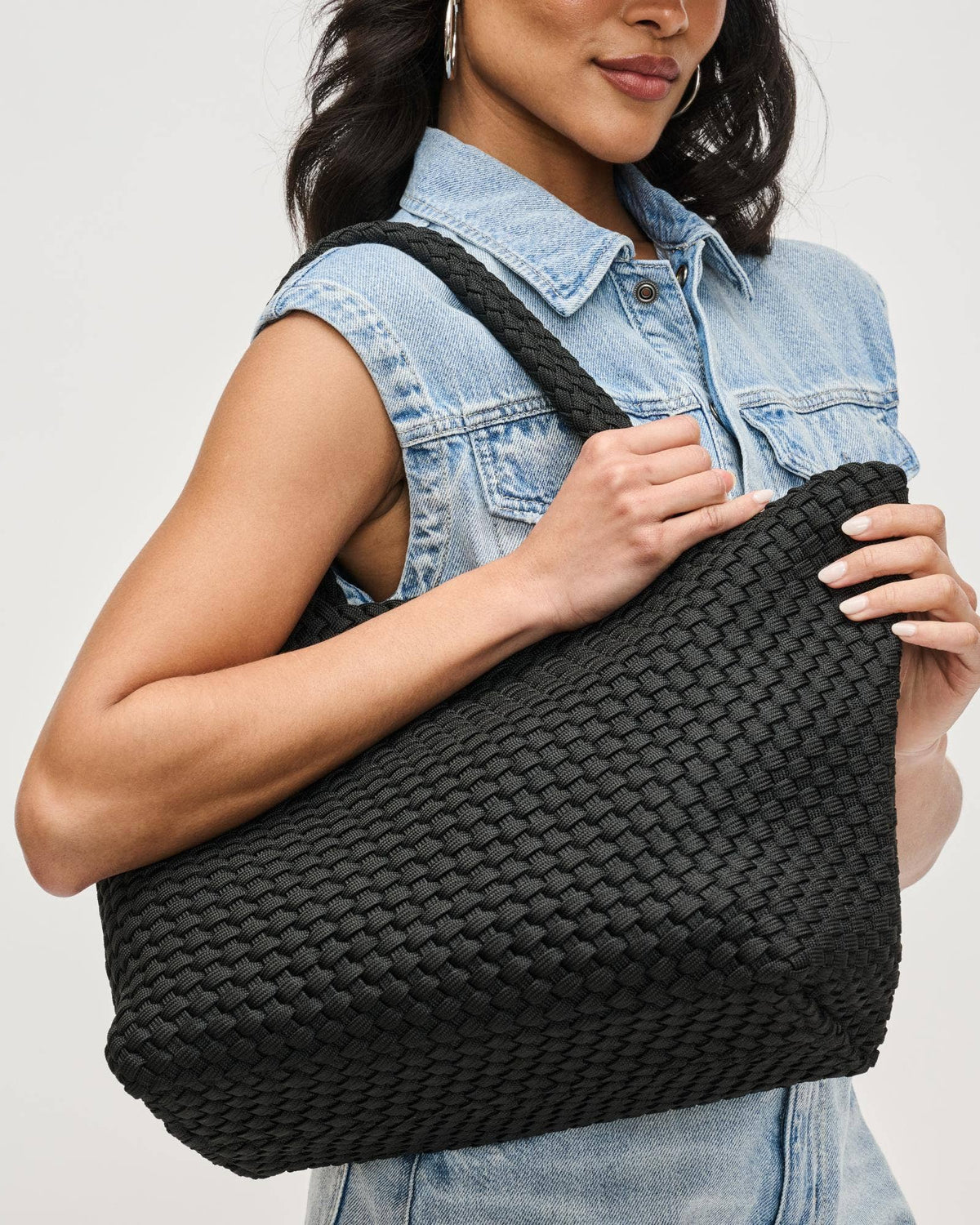 Woman holding a black woven handbag against a plain background