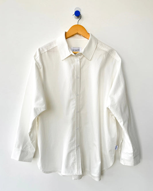 White button down shirt hanging on a wooden hanger against a white wall.