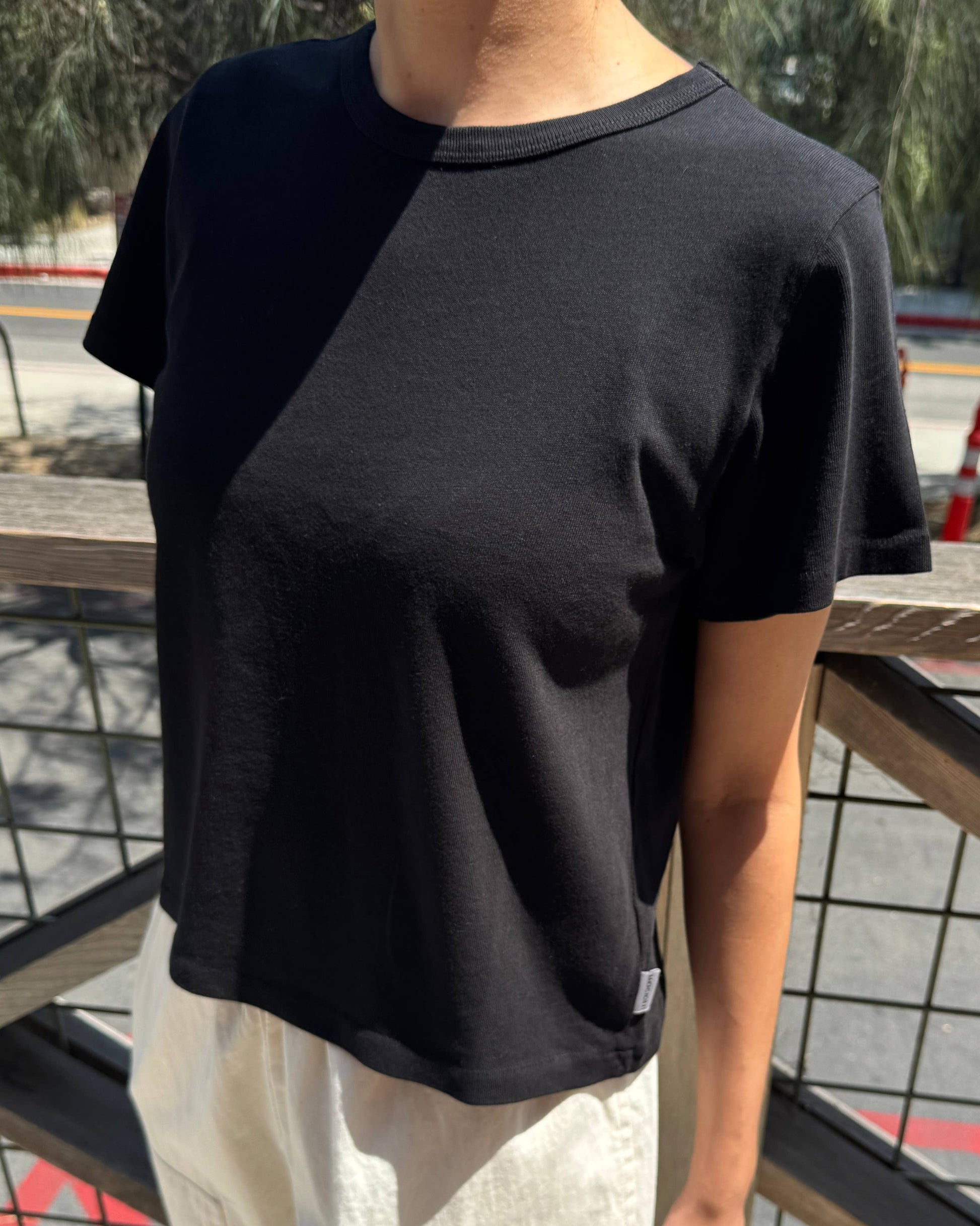 Person wearing a black t-shirt and light-colored pants standing outdoors.