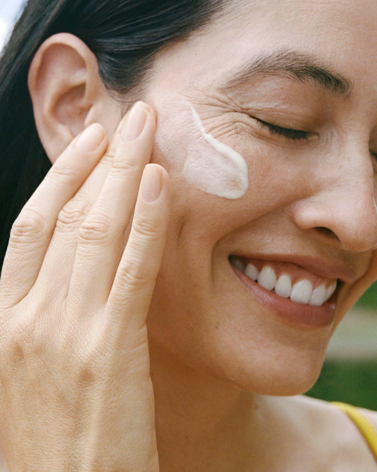 Woman applying cream to her face with a blurred green background