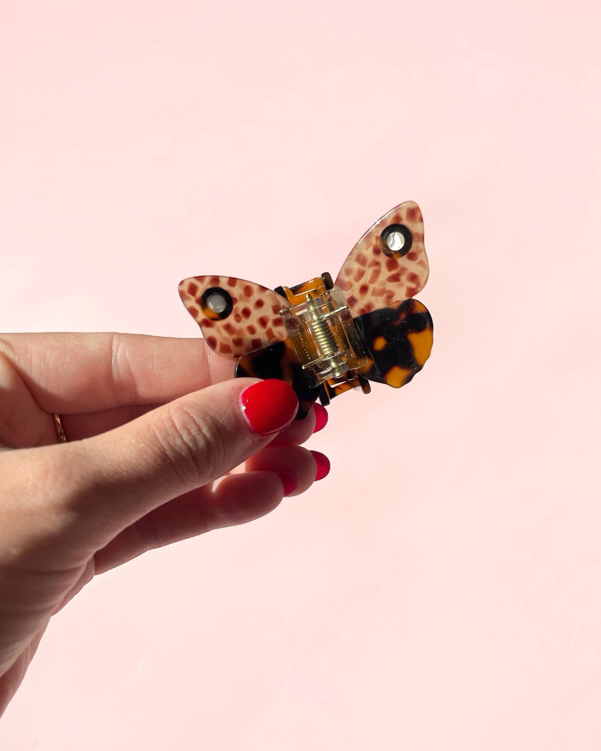Butterfly-shaped fidget spinner with leopard print design held by a hand on a pink background