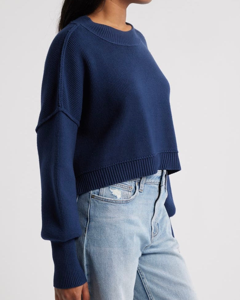 Side view of a model wearing the Free People Easy Street crop pullover sweater in navy standing against a white background.