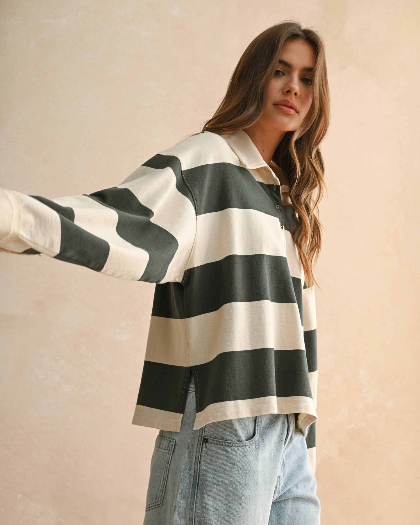 Woman wearing a green and white striped sweater with light blue jeans against a beige background