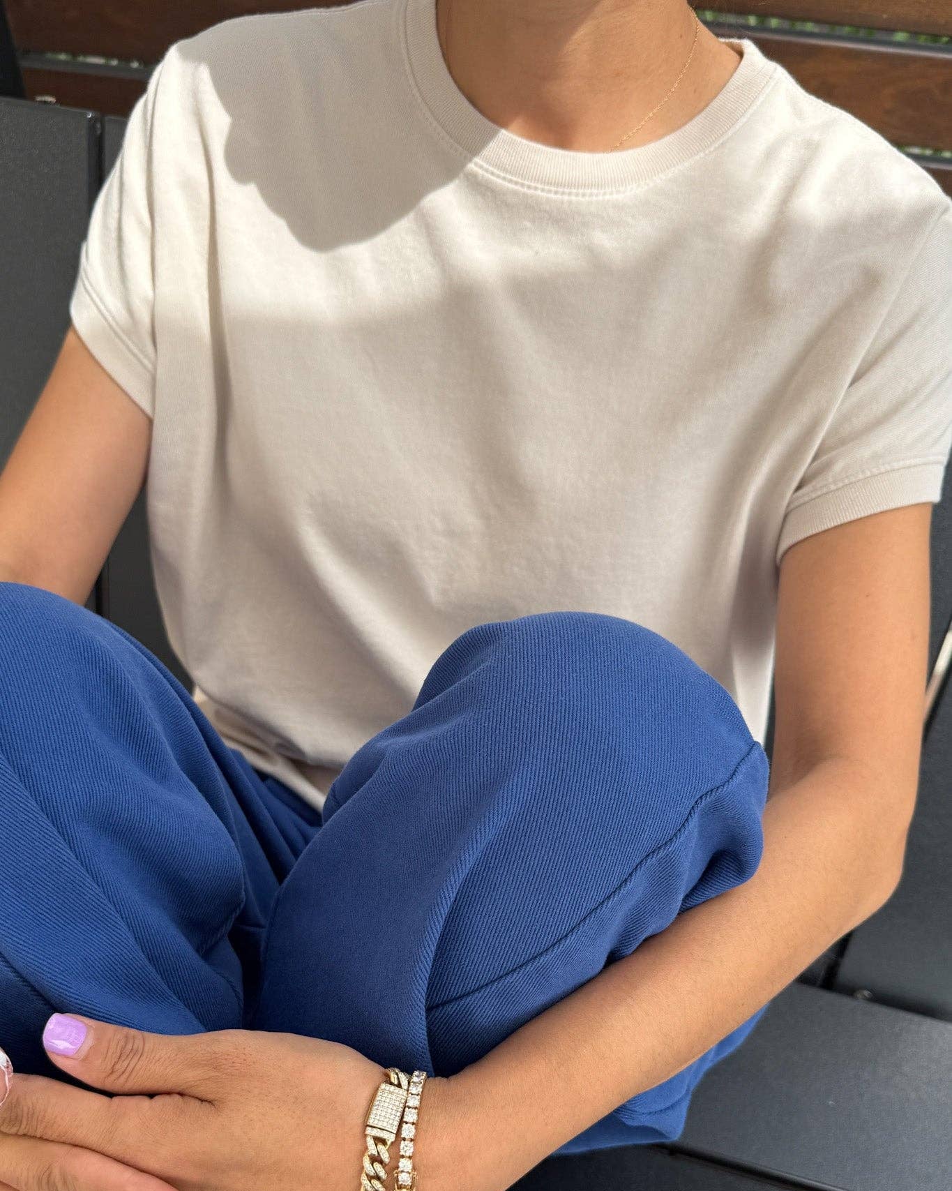 Person wearing a white t-shirt and blue pants sitting on a bench.