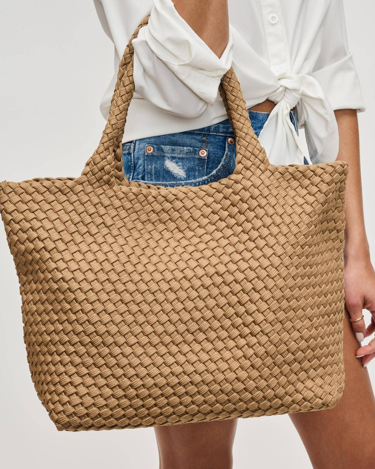 Person holding a woven beige tote bag against a plain background