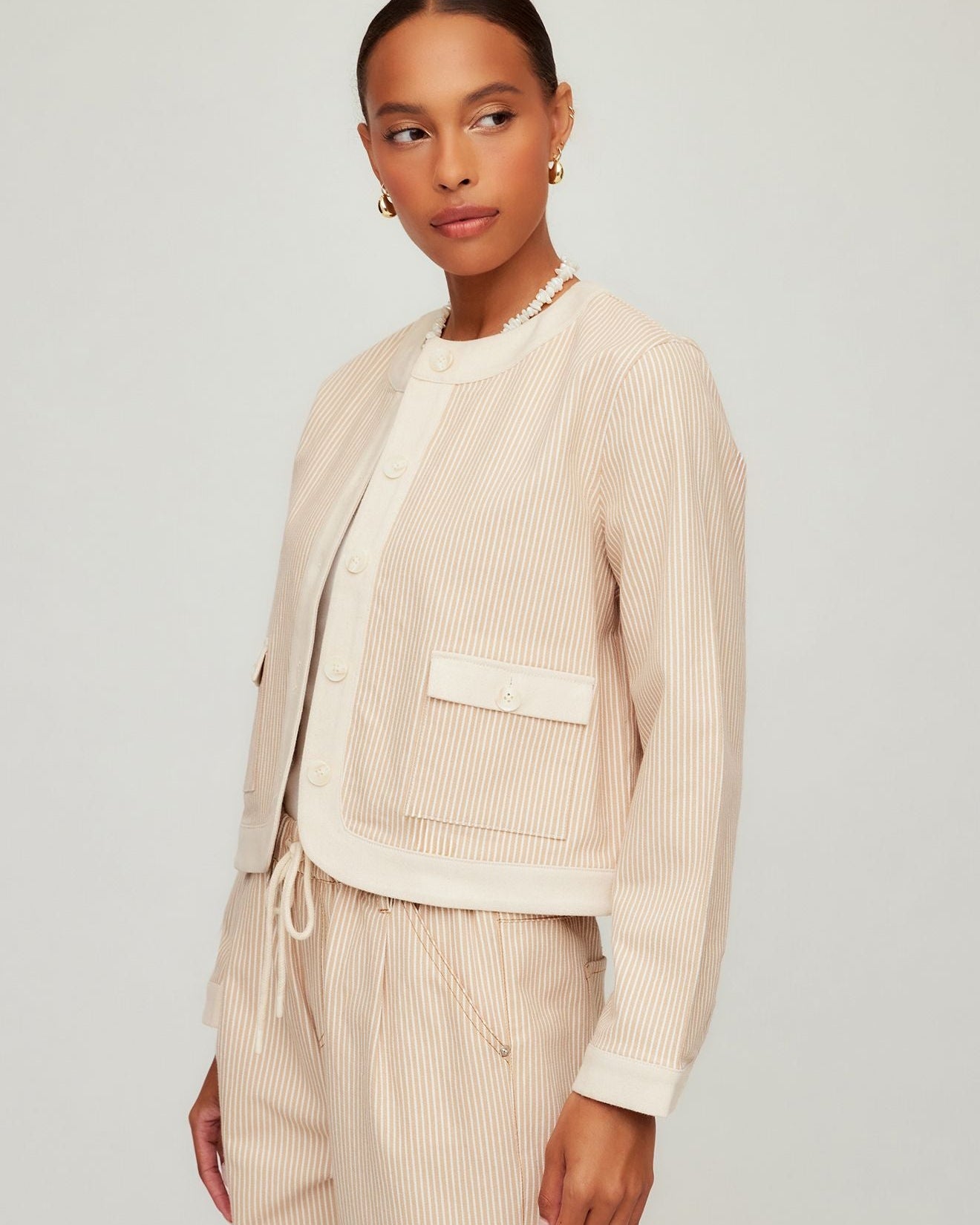 Woman wearing a beige ribbed cardigan over a matching top and pants on a light gray background