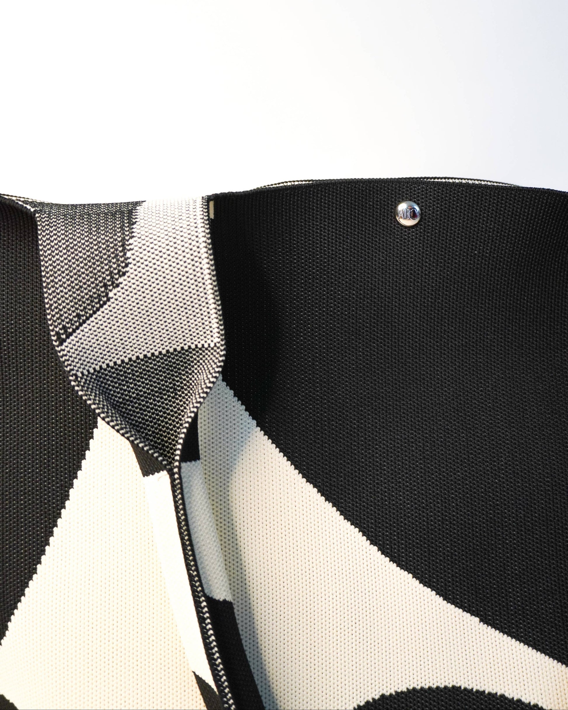 Close-up of a black and white patterned bag with a metallic clasp on a light gray background