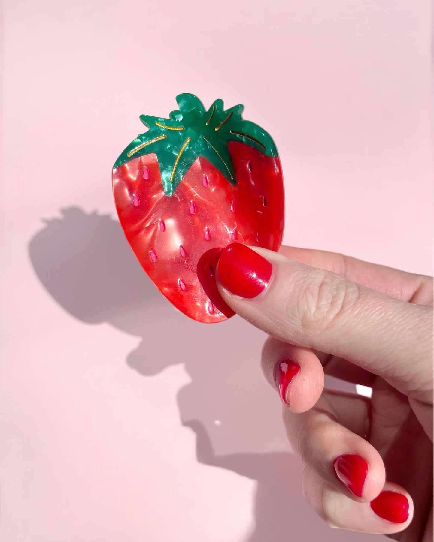 Hand holding a strawberry-shaped object against a pink background