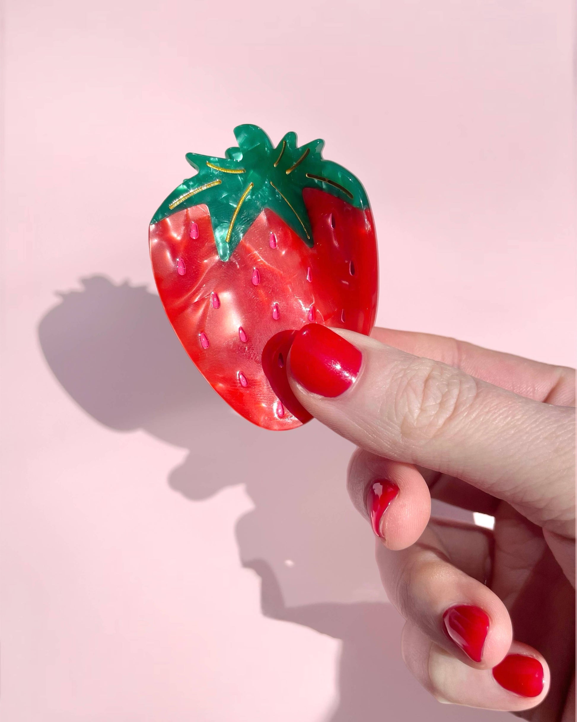 Hand holding a strawberry-shaped object against a pink background