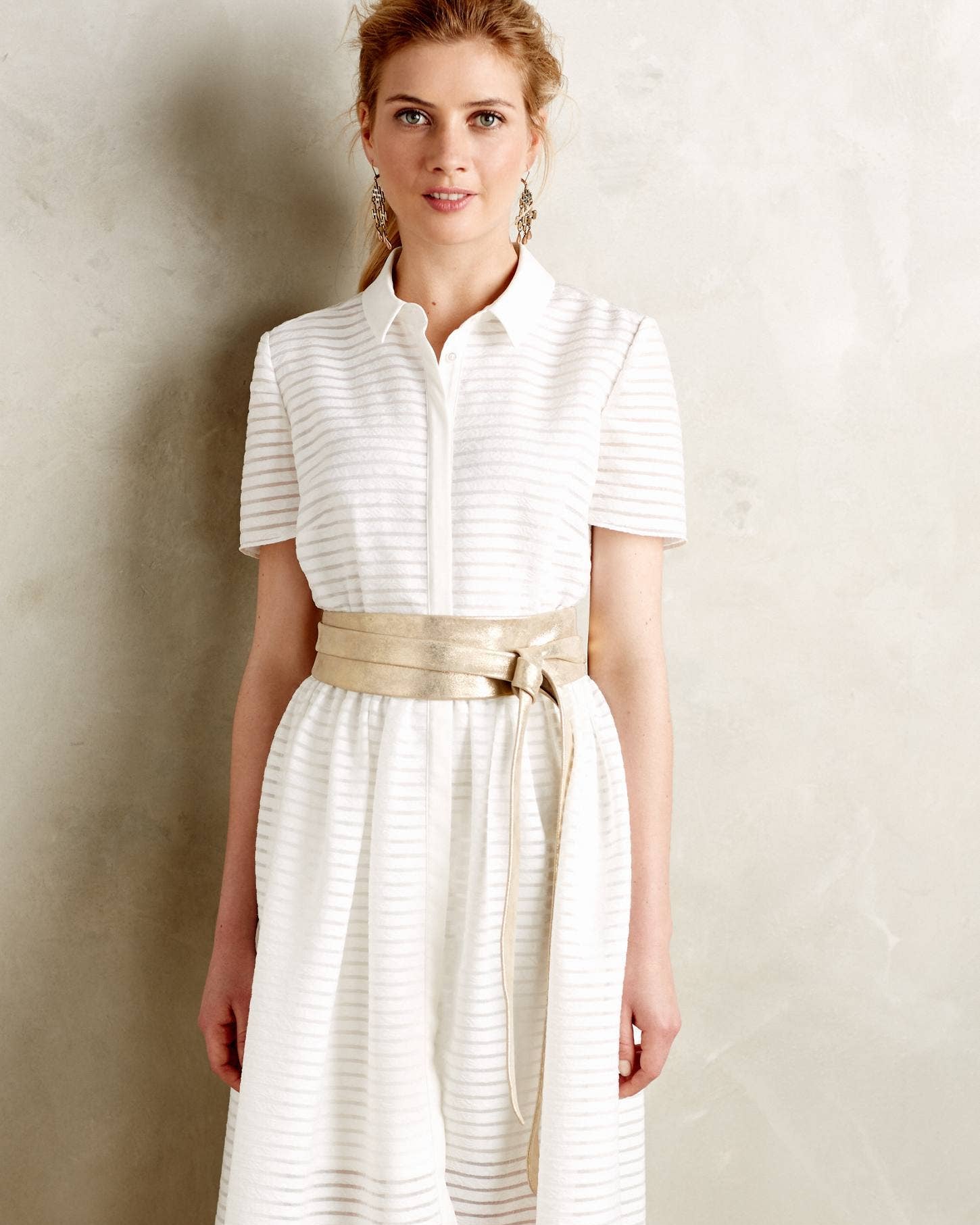 Woman wearing a white dress with a gold belt against a neutral background