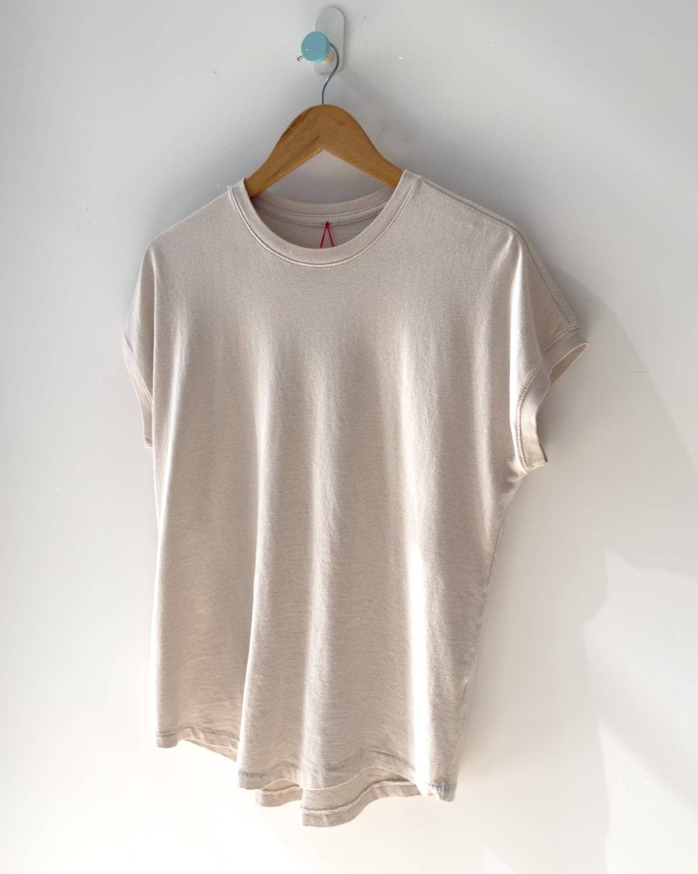 Beige t-shirt on a wooden hanger against a white wall