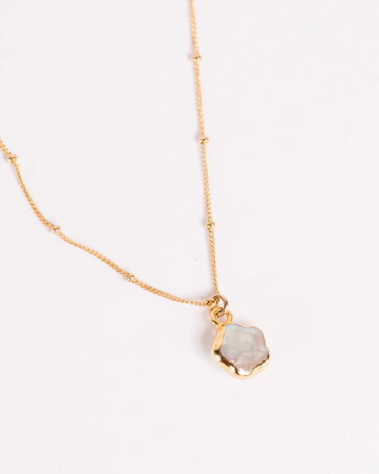 Close up of the Able Pearl Flower Pendant Necklace in gold laying against a white background.