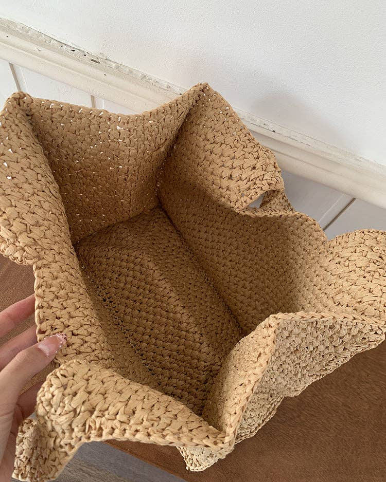 Close-up of a textured beige woven bag held by a hand against a neutral background