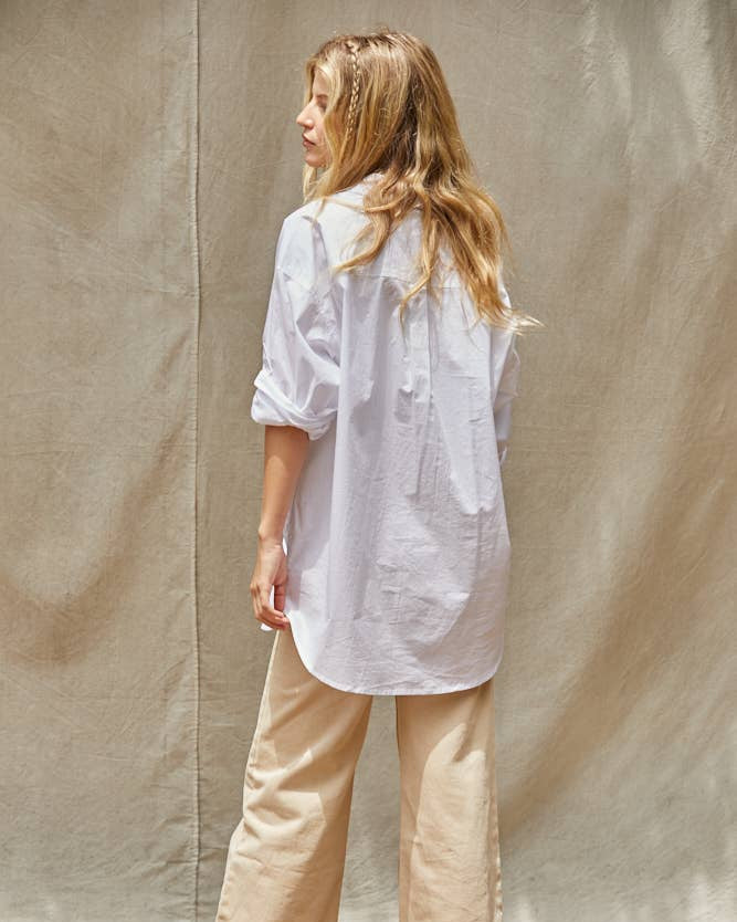 Woman wearing a white shirt and beige pants standing against a plain background