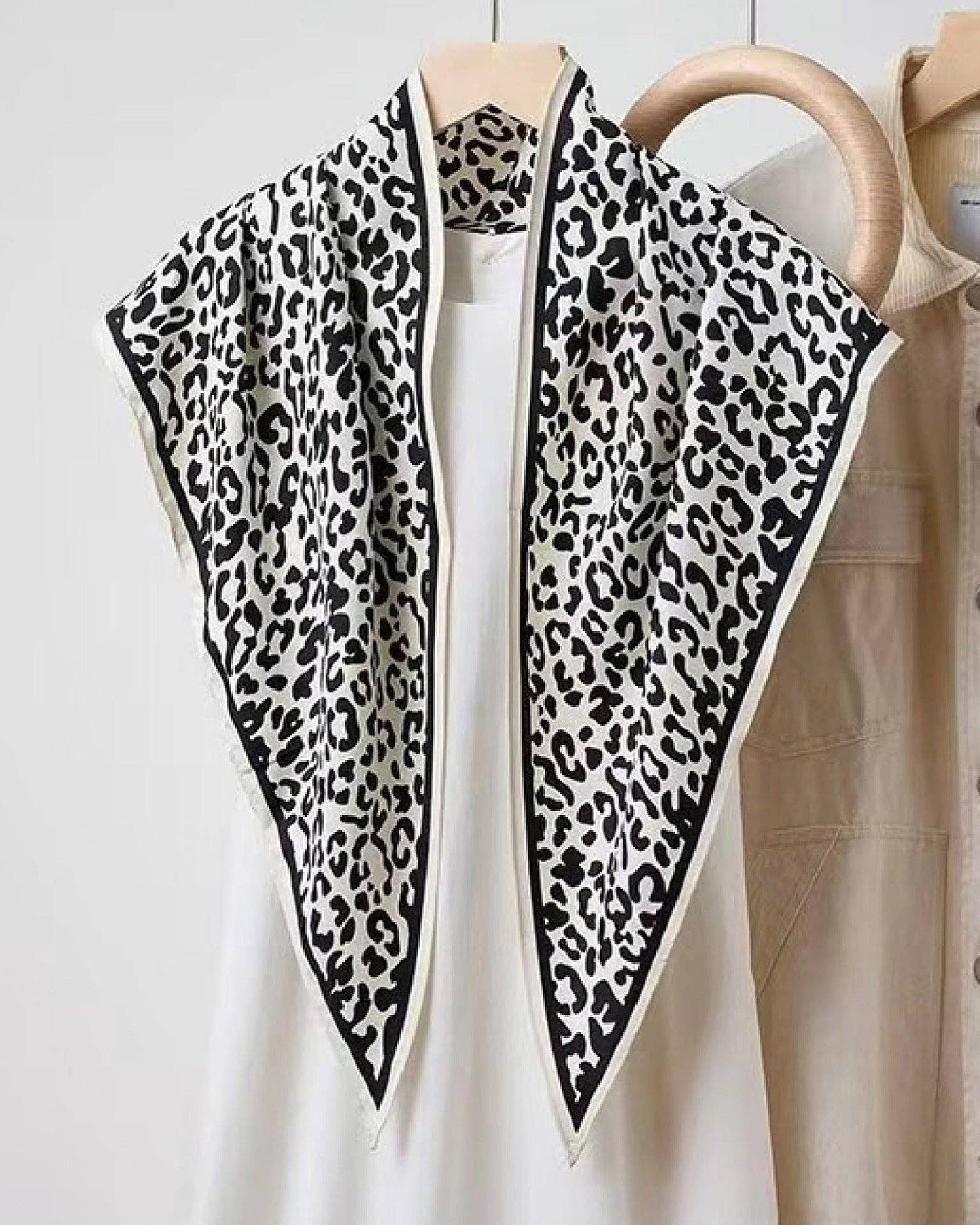 Leopard print scarf draped over a white shirt with a beige jacket in the background.