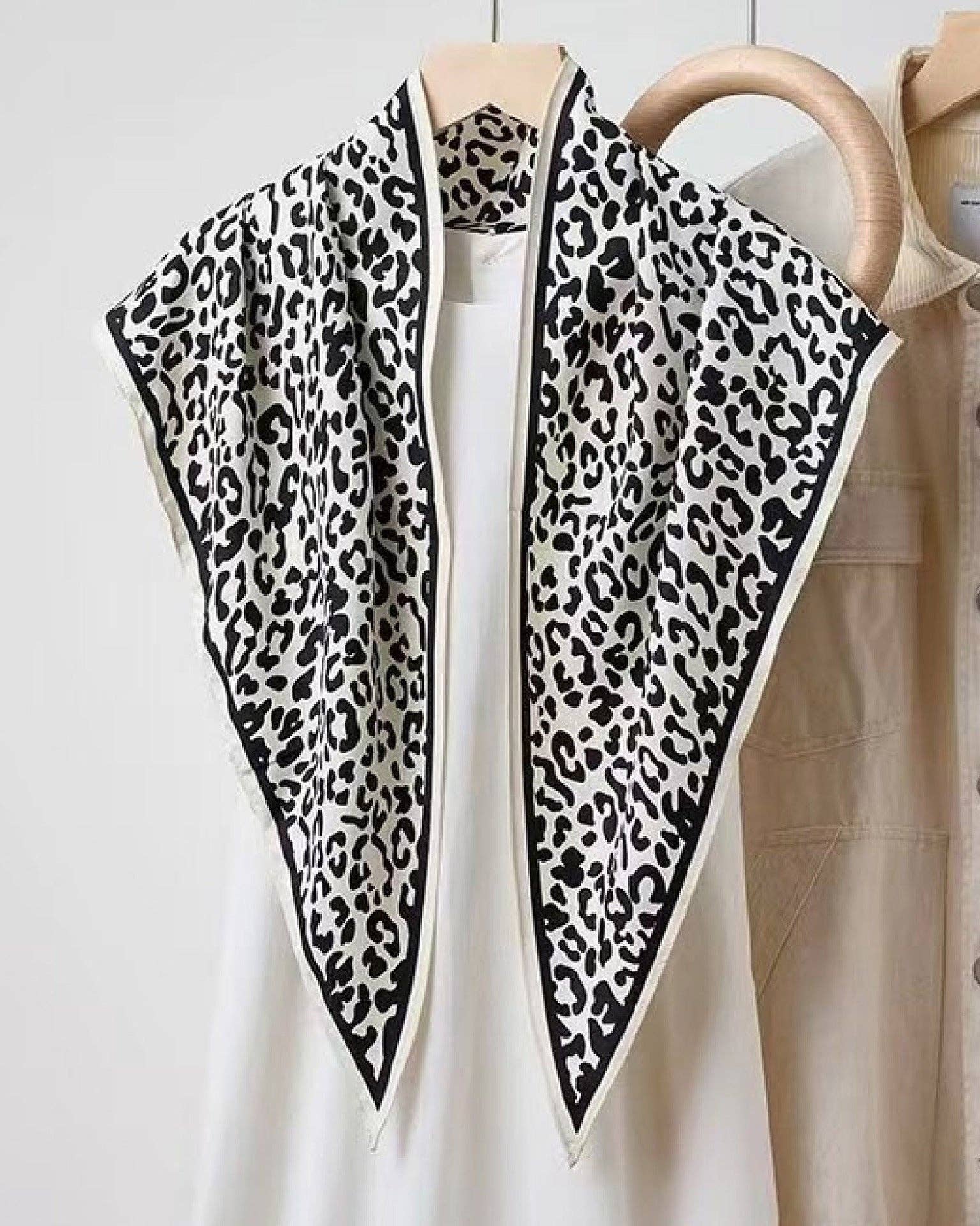 Leopard print scarf draped over a white shirt with a beige jacket in the background.