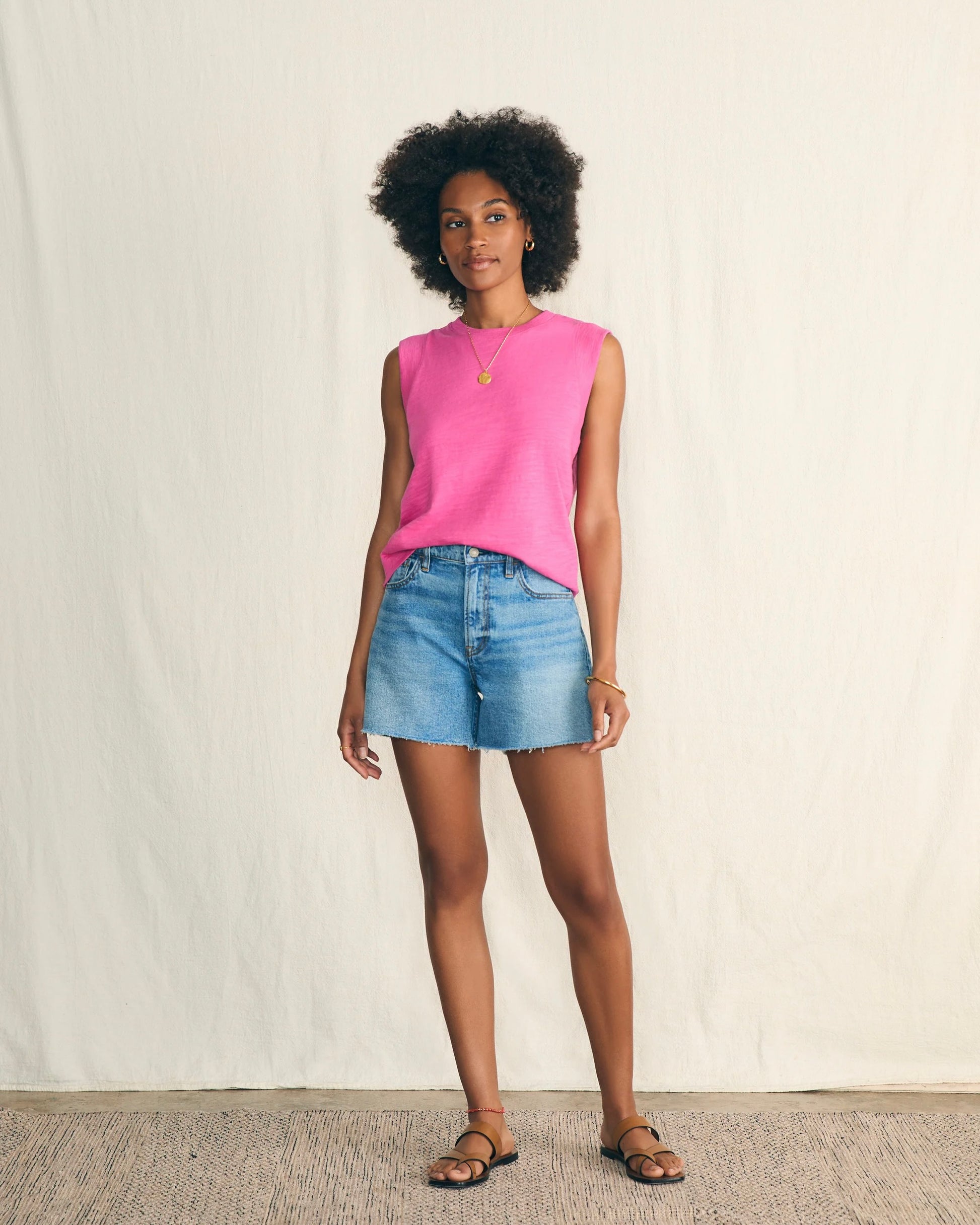 Model wearing Faherty Sunwashed Sub Muscle Tank in Cone flower pink wearing jean shorts on a white background