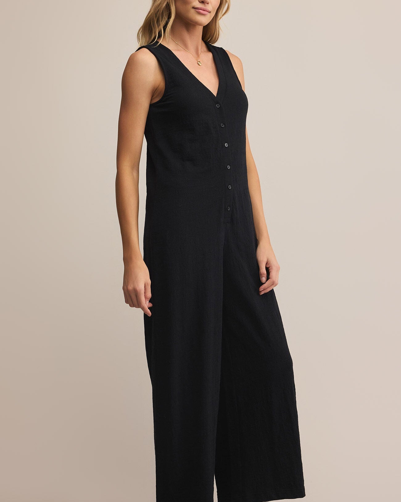Woman wearing a black sleeveless jumpsuit on a beige background