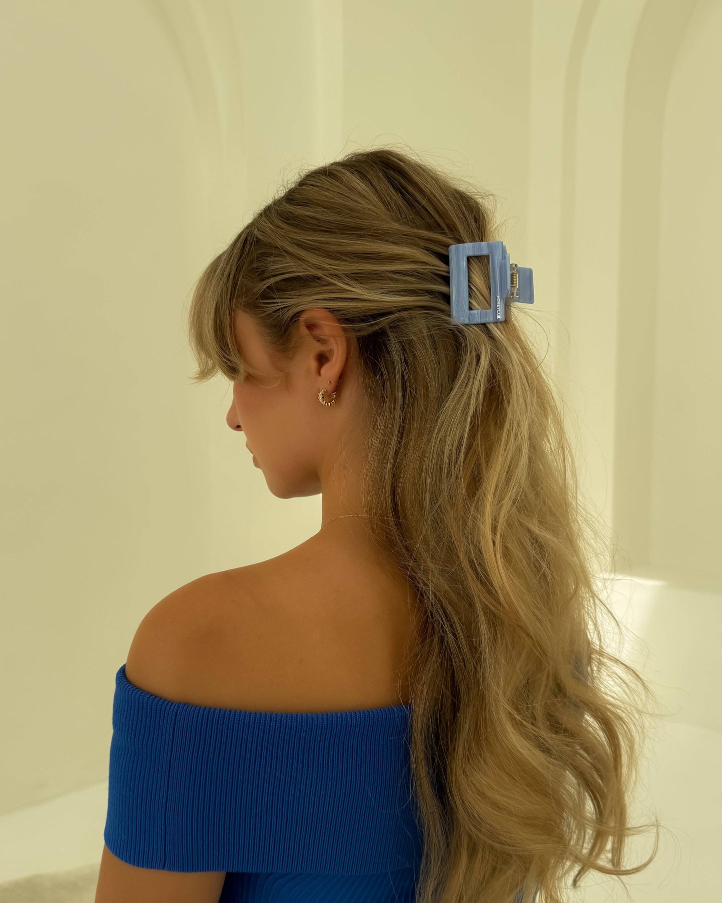 Woman with long blonde hair tied back with the HoneyLux Ecofriendly Acetate Midi Clip in the color Amalfi, wearing an off-shoulder blue top.
