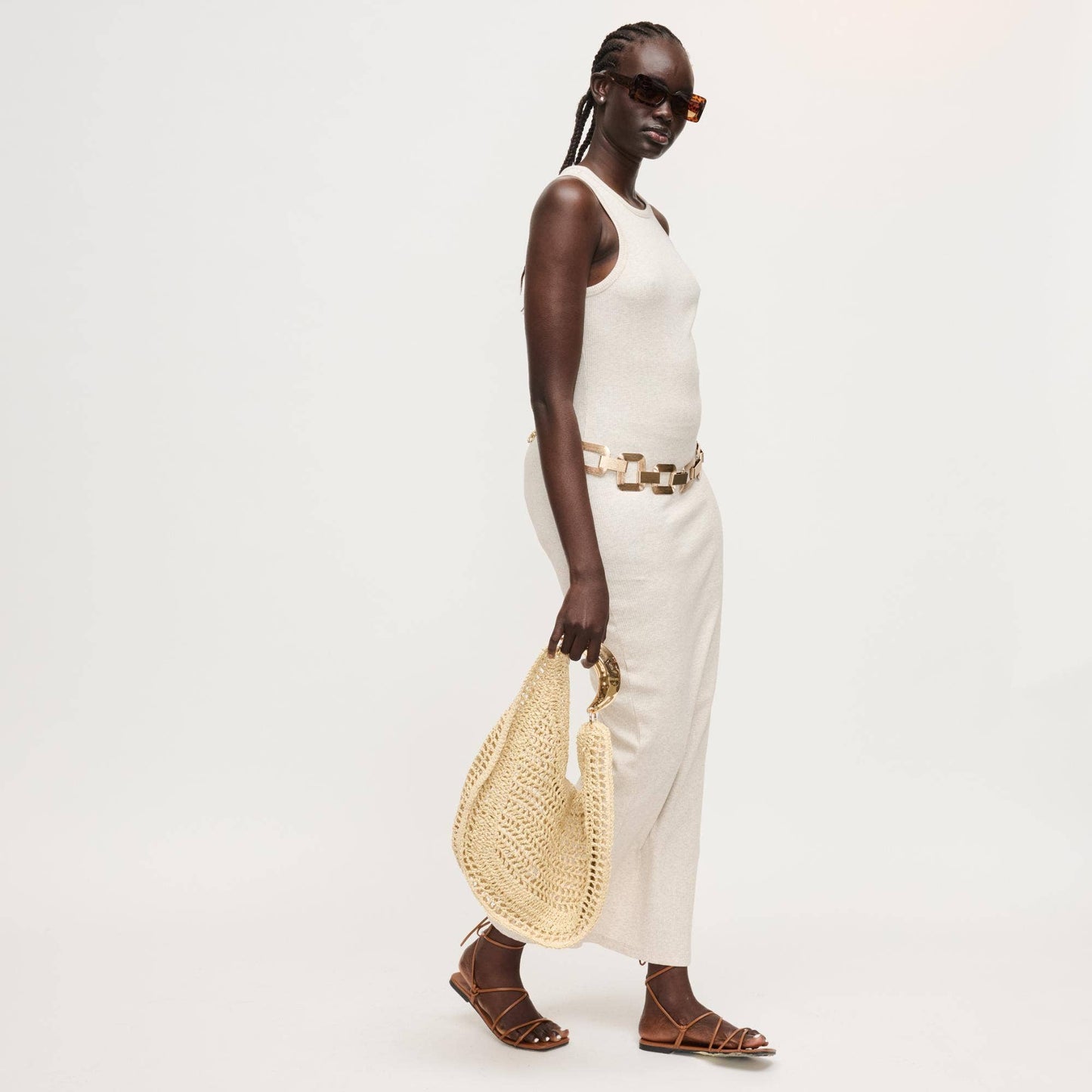 Woman in white outfit holding a straw bag on a plain background
